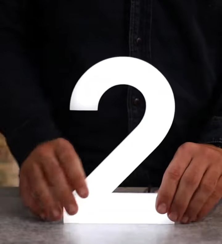 Mãos a acertar um número 2 em acrílico branco na bancada